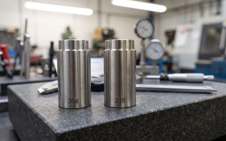 Two CNC machined stainless steel components marked 304 and 316 side by side on a granite inspection plate