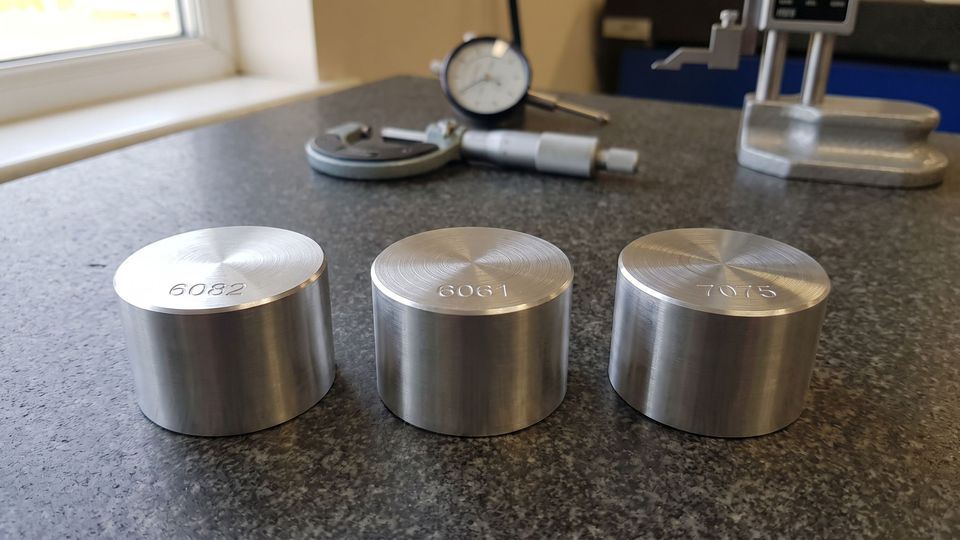 Three CNC machined aluminium discs engraved 6082, 6061 and 7075 side by side on a granite inspection plate