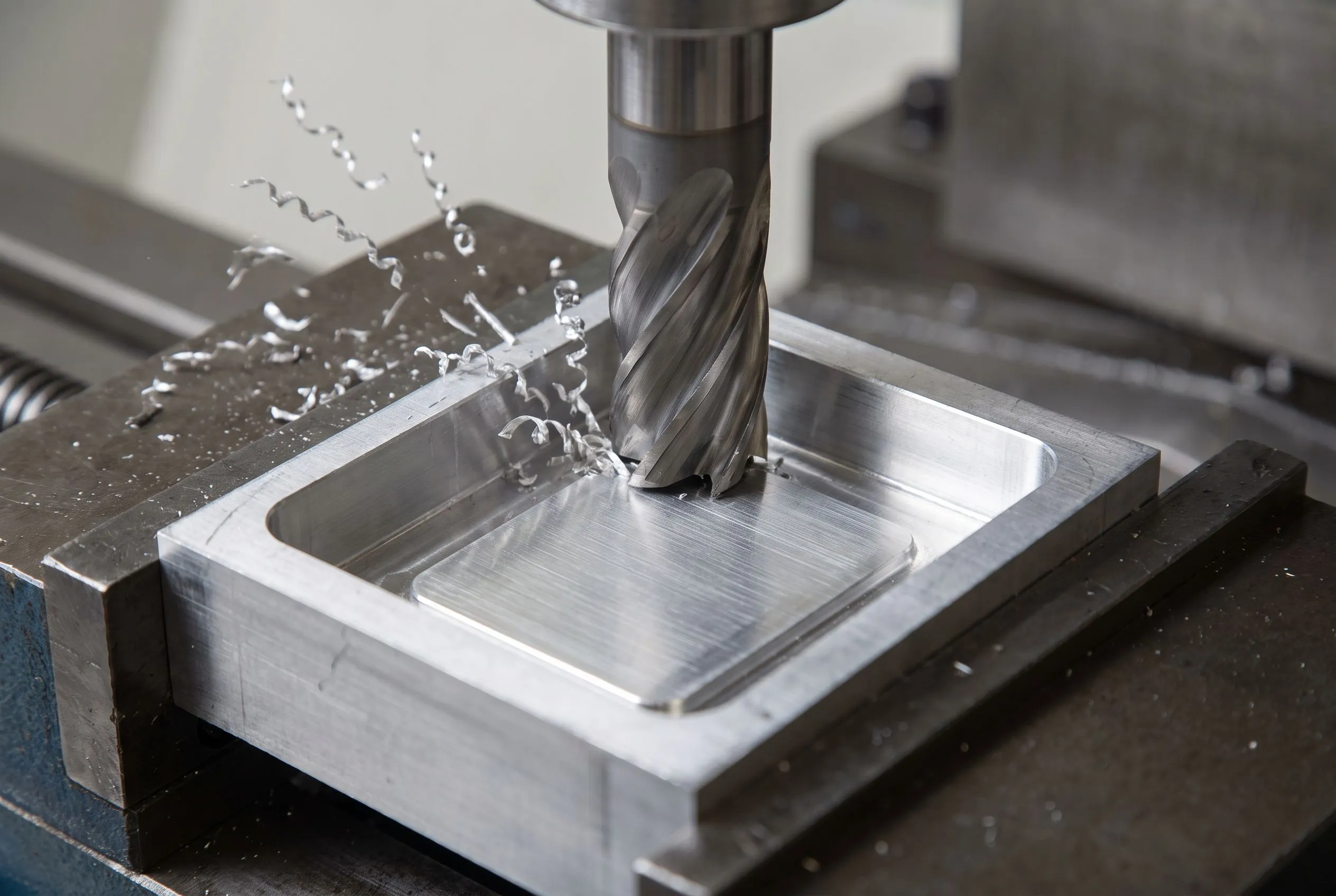 Carbide end mill machining a pocket in aluminium plate held in a machine vice, with chips clearing from the cut