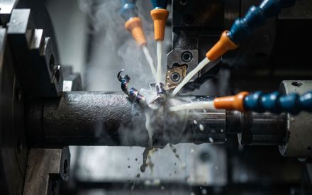 CNC lathe machining a nickel alloy bar under high-pressure flood coolant with heat-tinted chips curling away